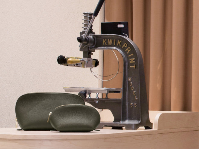Two pouches on a wooden surface next to a metal stamping machine.