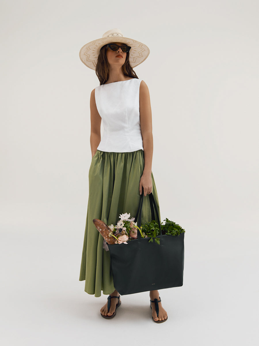 Person wearing a sleeveless top, long skirt, hat, and sunglasses, holding a large bag with groceries.