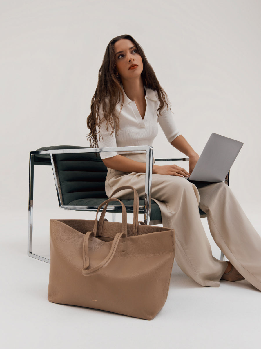 Woman sitting on chair with laptop, large bag on the floor in front of her