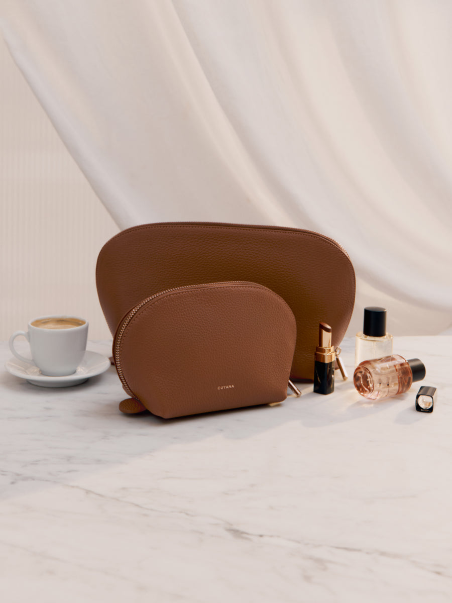 Two cosmetic pouches, cup of coffee, lipstick, perfume bottle, and a small container on a marble surface