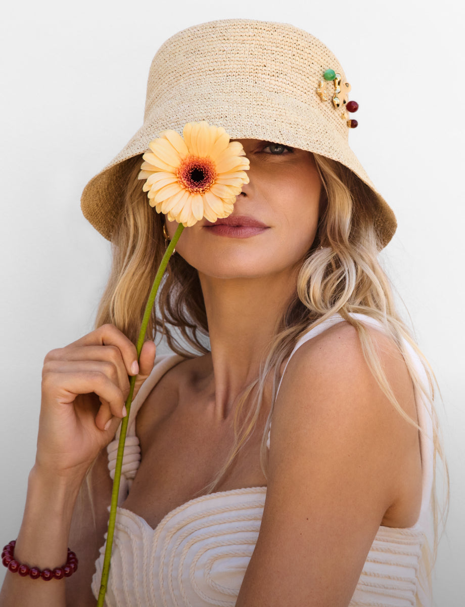 Person with a bucket hat holding a flower up to their face.