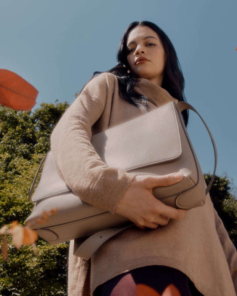 Person holding a large handbag, looking up with trees in the background.