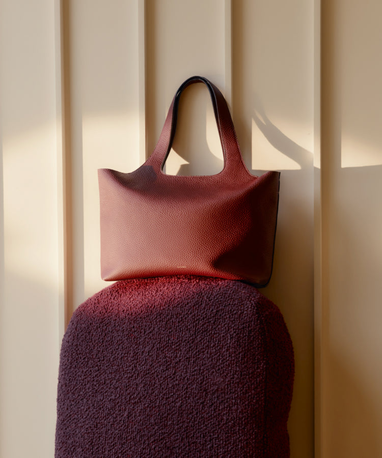 A handbag is placed on a soft-textured surface against a paneled wall.