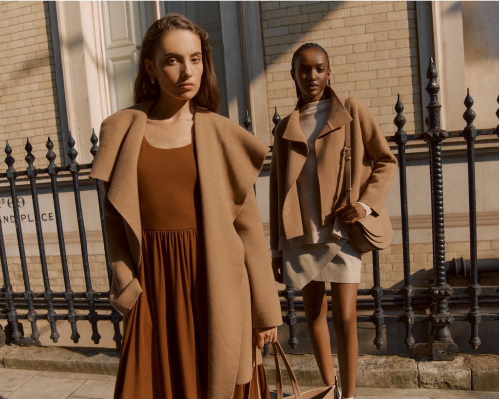 Two women standing by a fence, one holding a bag.