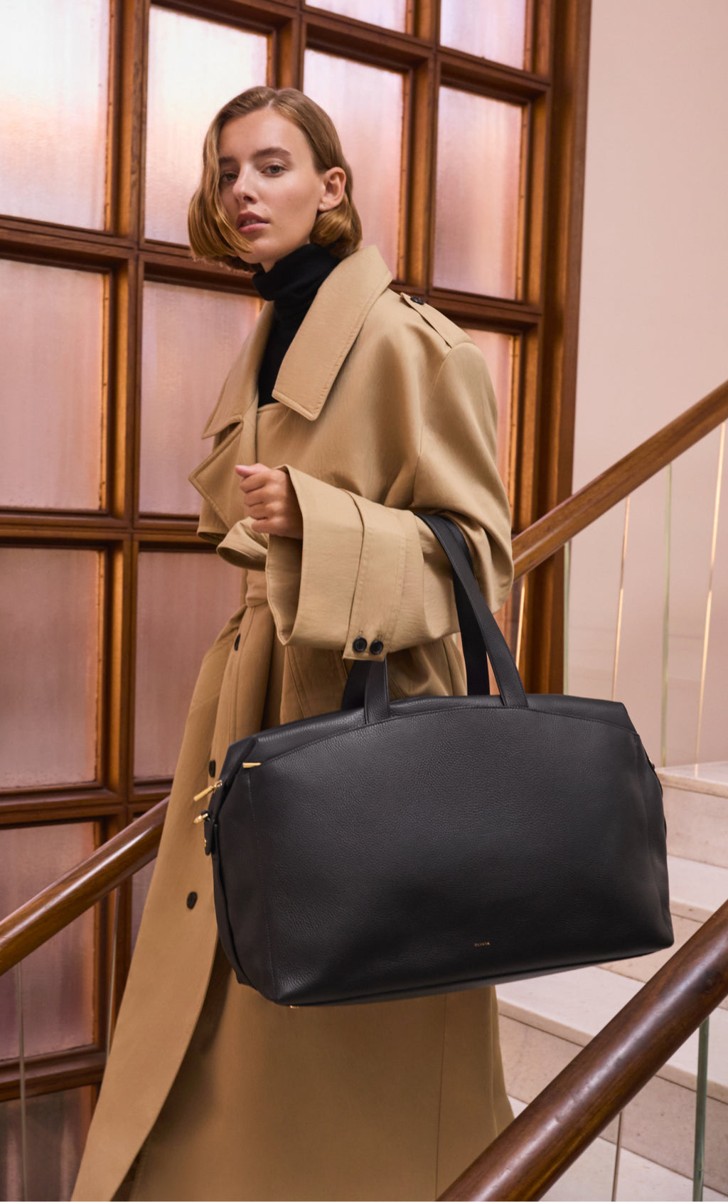 Person in long coat carrying a travel bag, standing on stairs.