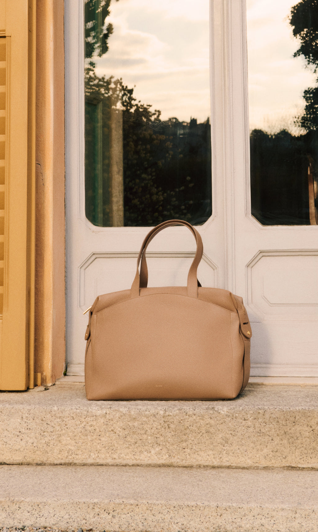Travel bag on stone step in front of glass doors.