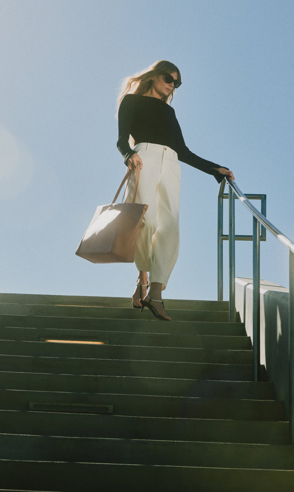 Person walking down stairs holding a large bag and wearing sunglasses.