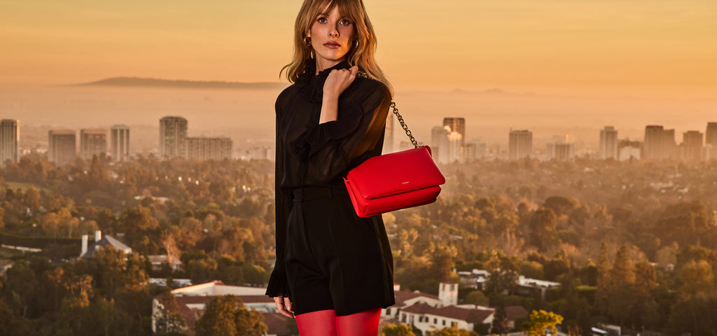 Person in a dress holding a handbag with a cityscape in the background.