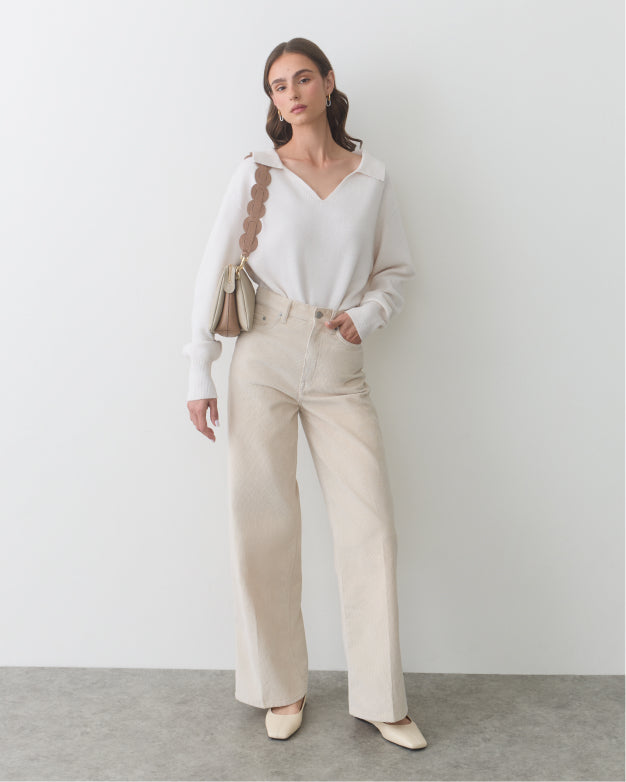 Person in casual outfit with a purse over shoulder standing in a room.