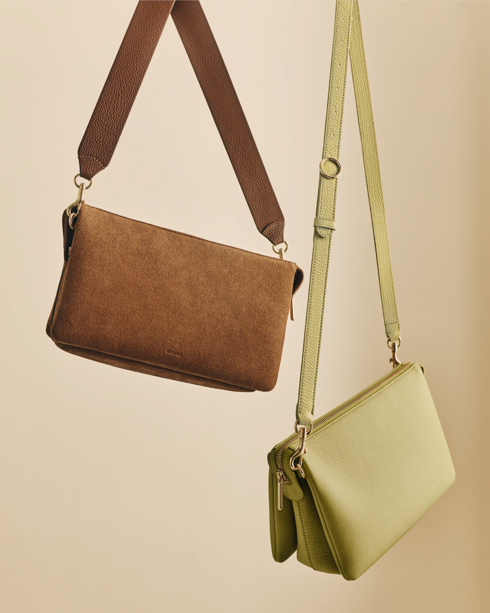 Two handbags with long straps are suspended against a plain background.