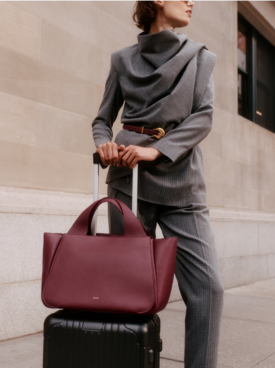 Person in a stylish outfit holding a suitcase handle with a travel bag on top.