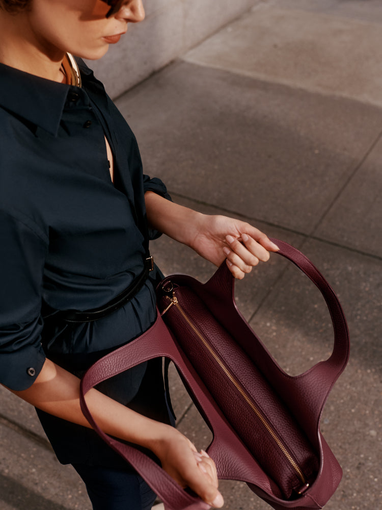 Person holding a handbag with a zipper, standing on a pavement.