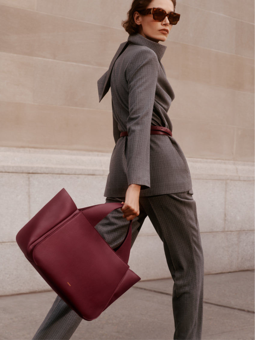 Person wearing a suit, sunglasses, carrying a large handbag over shoulder.