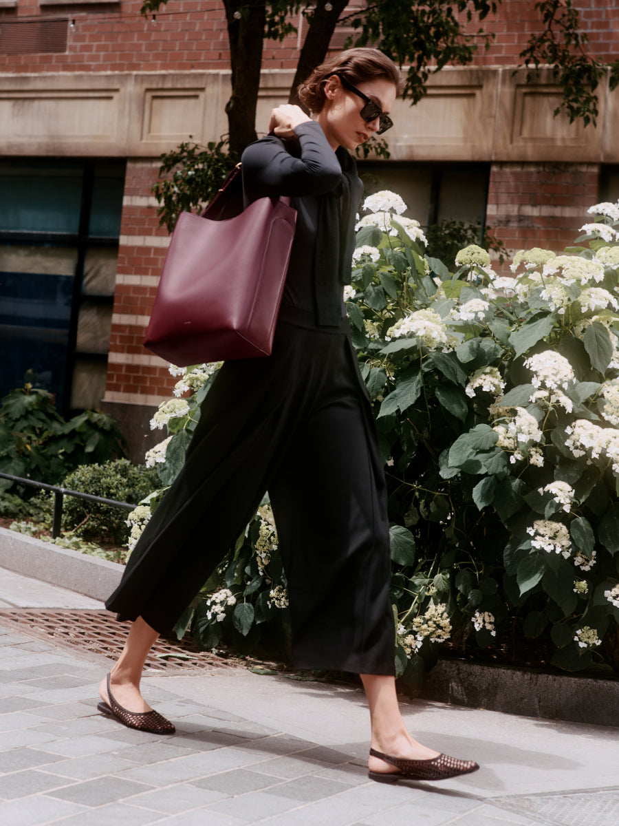 Person walking on a sidewalk carrying a shoulder bag.