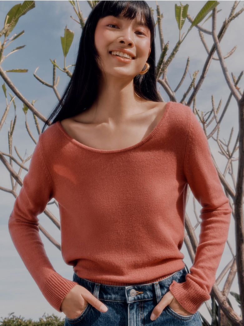 Woman in a sweater smiling with her hands in jeans pockets, standing outdoors.