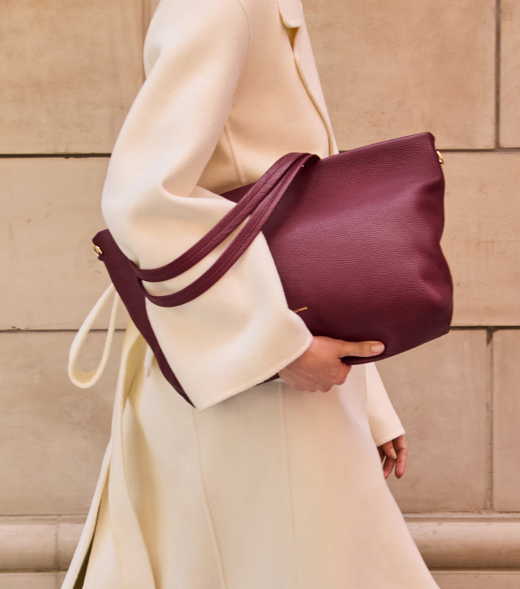 Person in coat holding a large handbag with shoulder straps