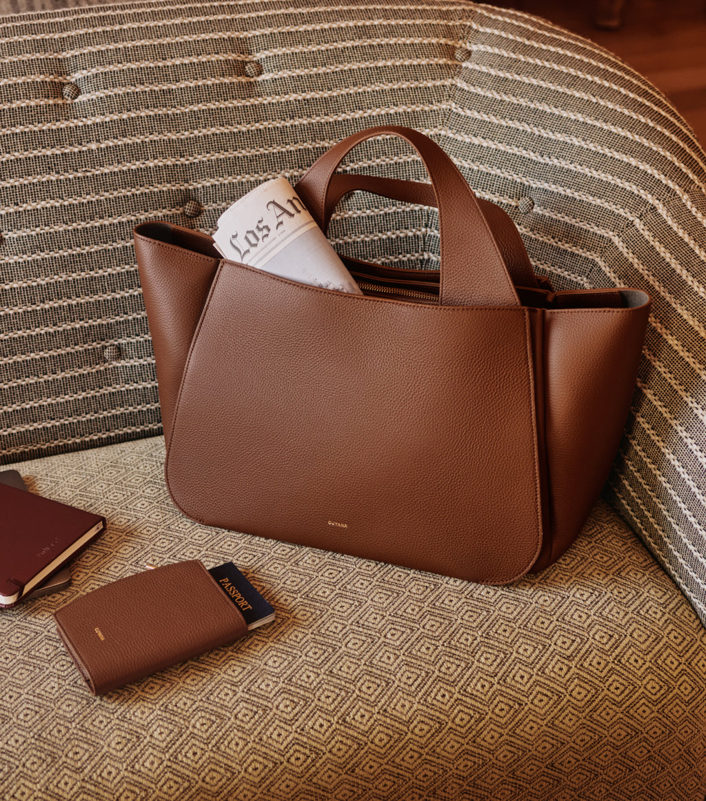Travel bag on sofa with a magazine and passport holder nearby