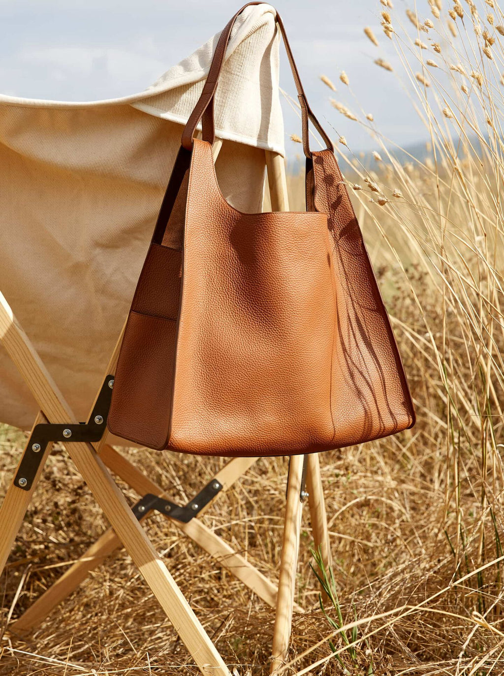 A handbag hanging on a folding chair in a field with tall grasses.