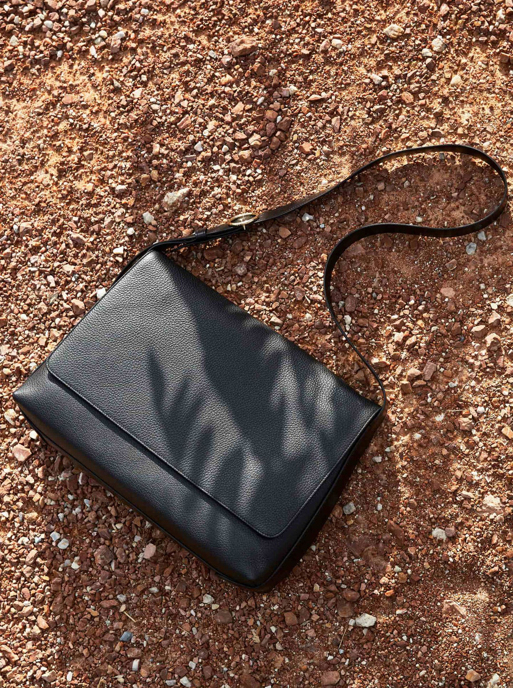 Purse with a strap lying on a textured ground.
