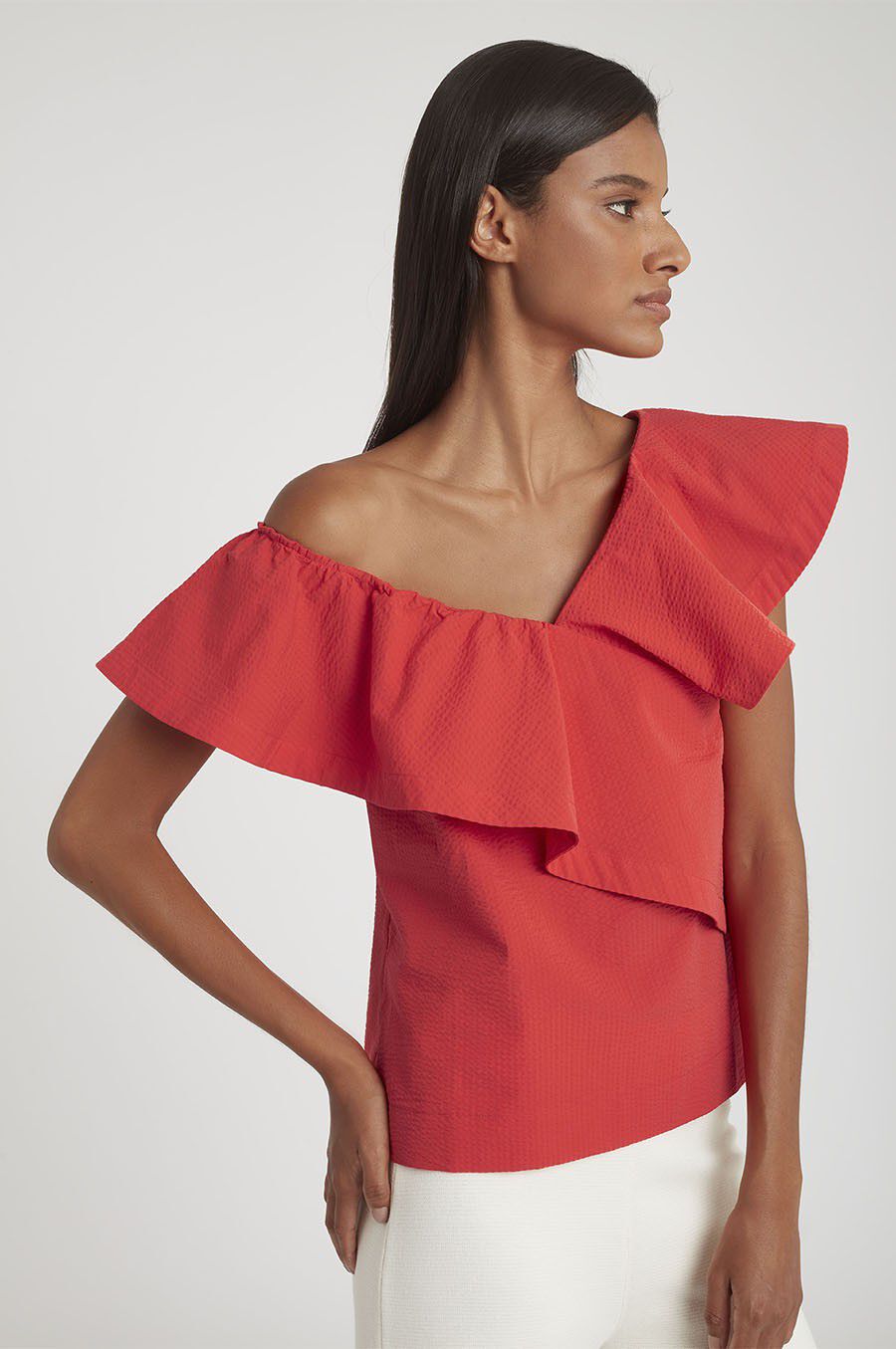 Woman in an off-shoulder top with layered ruffles, standing sideways.