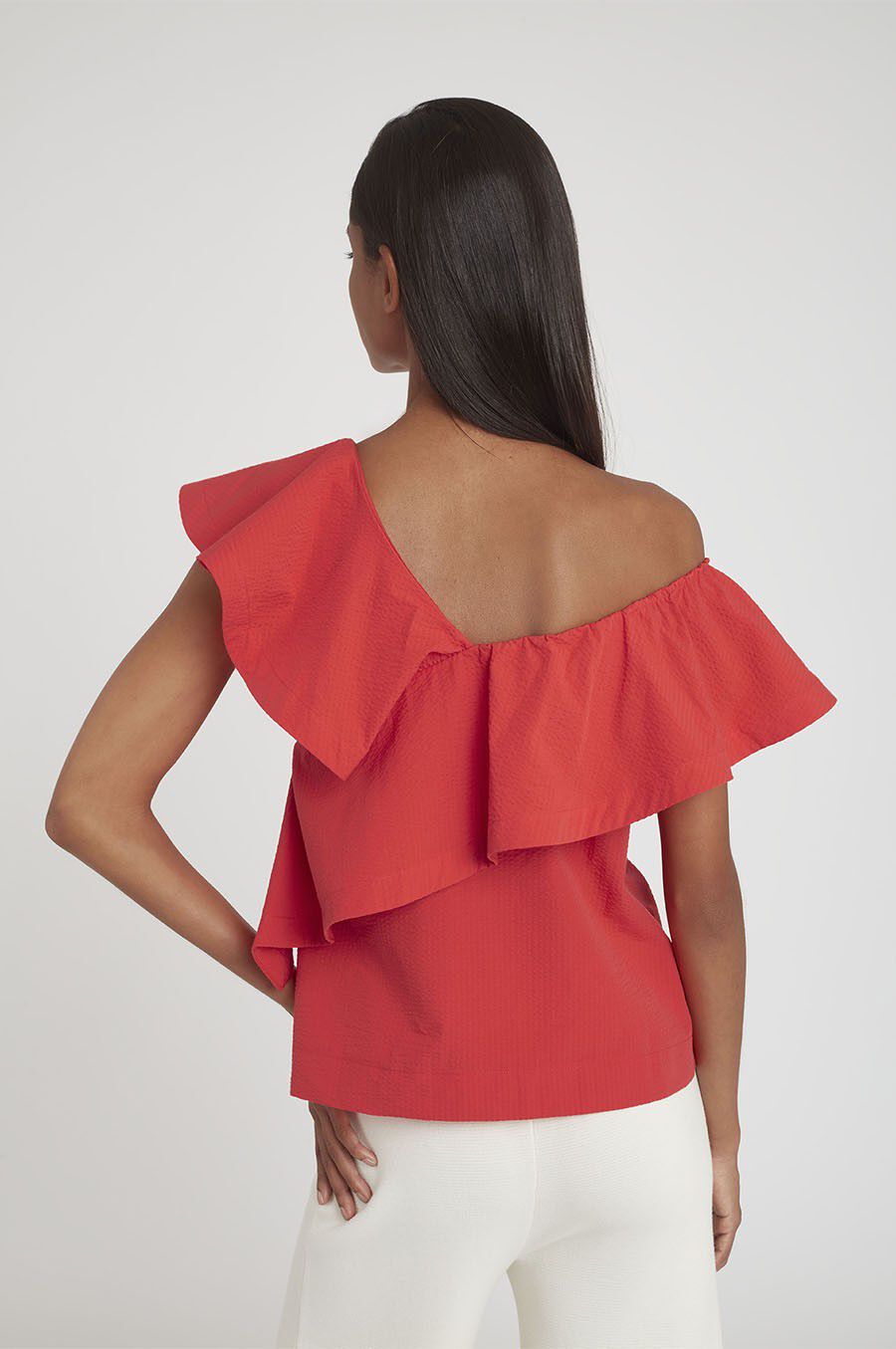 Woman from behind wearing a ruffled top and white pants.