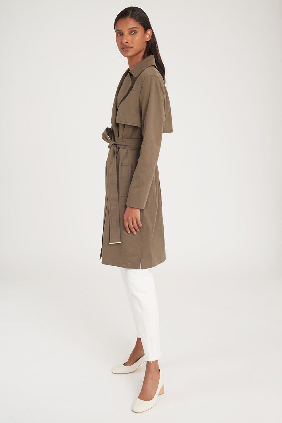 Woman standing side profile in a trench coat and pants.