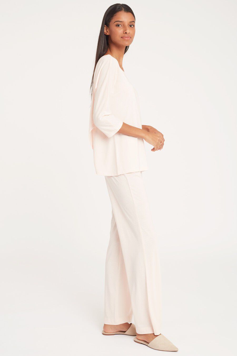 Woman standing in profile wearing a long-sleeve top and pants.