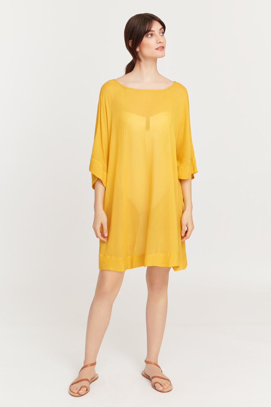 Woman standing and looking sideways in a casual dress and sandals.