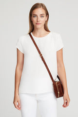 Woman standing with a shoulder bag, wearing a short-sleeved top and pants.