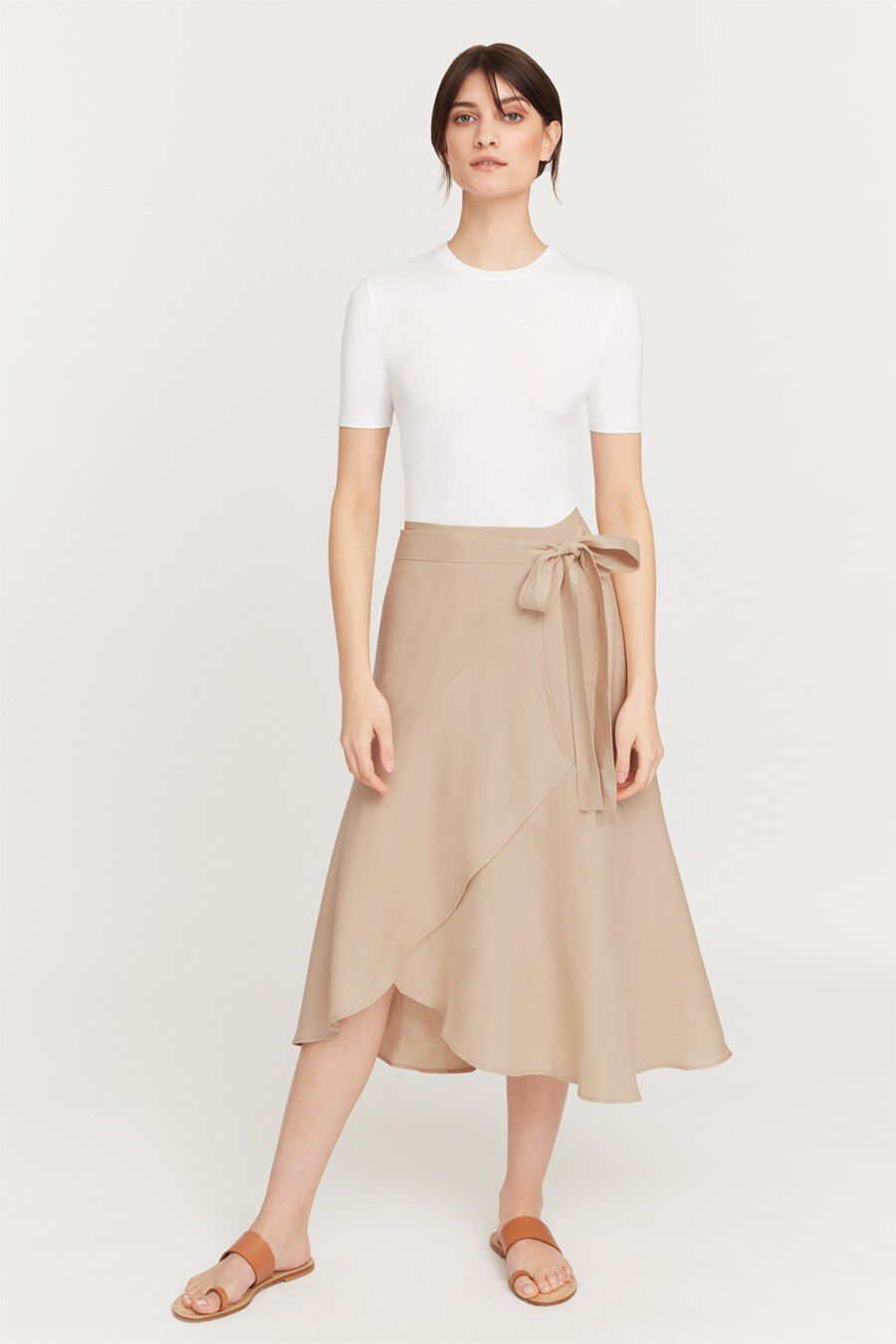 Woman standing in a plain short sleeve top and mid-length skirt with sandals.