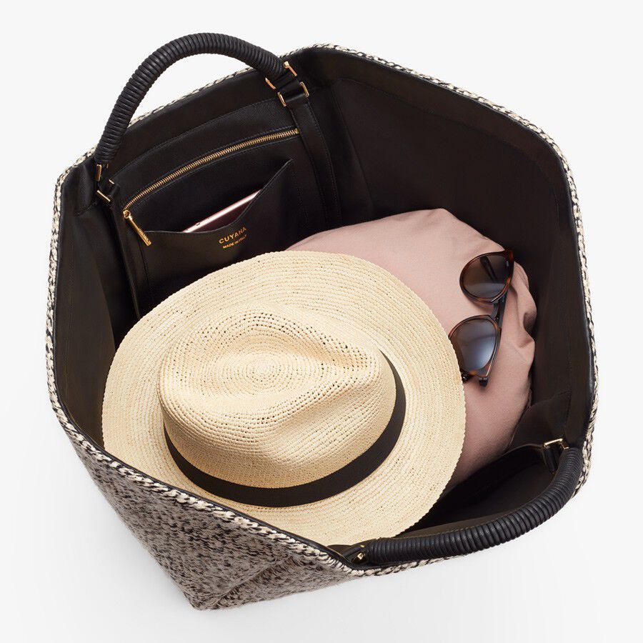 Top view of an open bag containing a hat, sunglasses, and a towel.