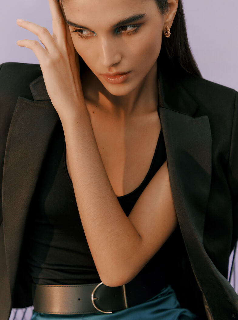 Woman posing with hand on forehead, wearing a blazer and tank top.