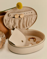 Open round jewelry case with earrings and a jewelry pouch inside, next to a flower.