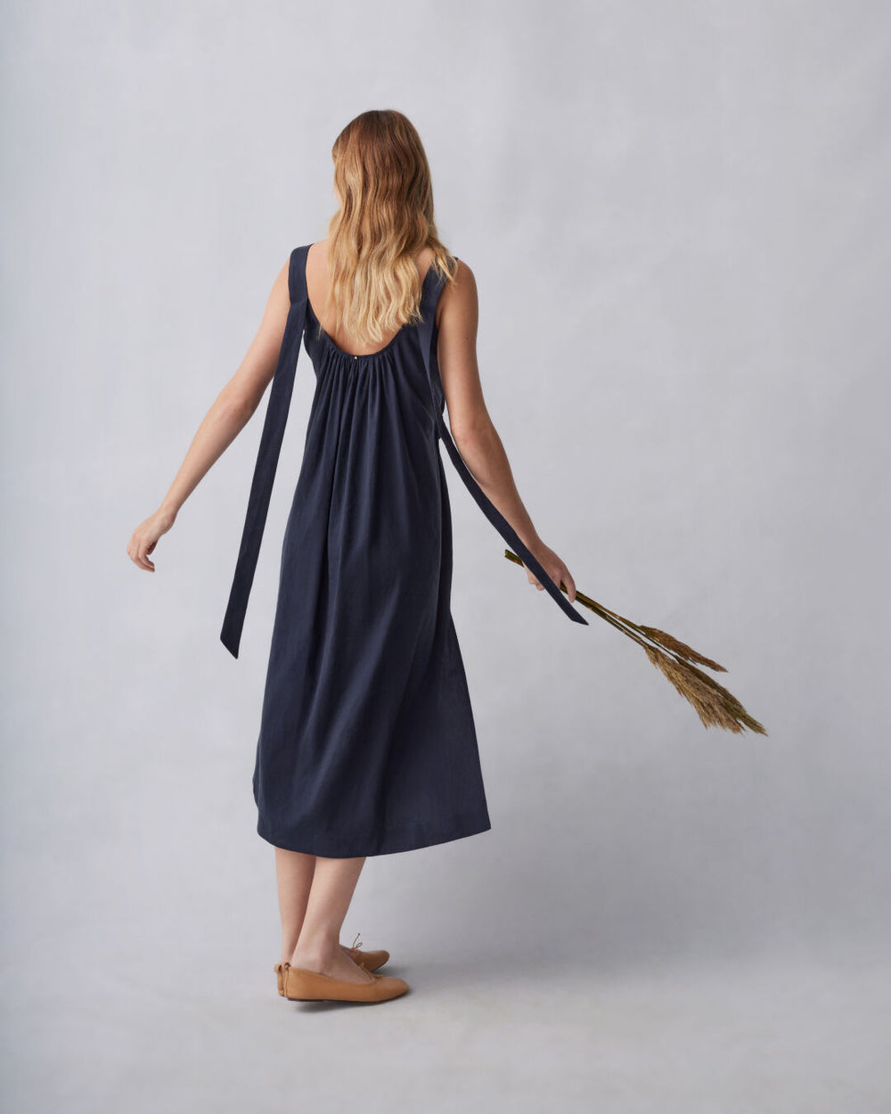 Woman in a dress holding a broom, walking away from the camera.