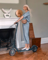 Woman standing with an electric scooter in a room with a fireplace.