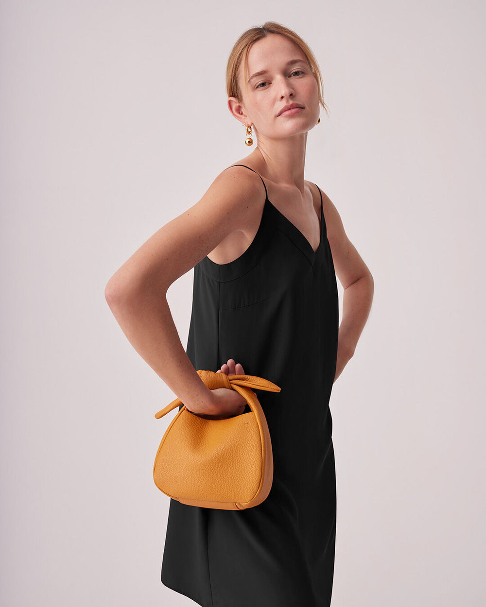 Woman posing with her hand on her hip, holding a purse.