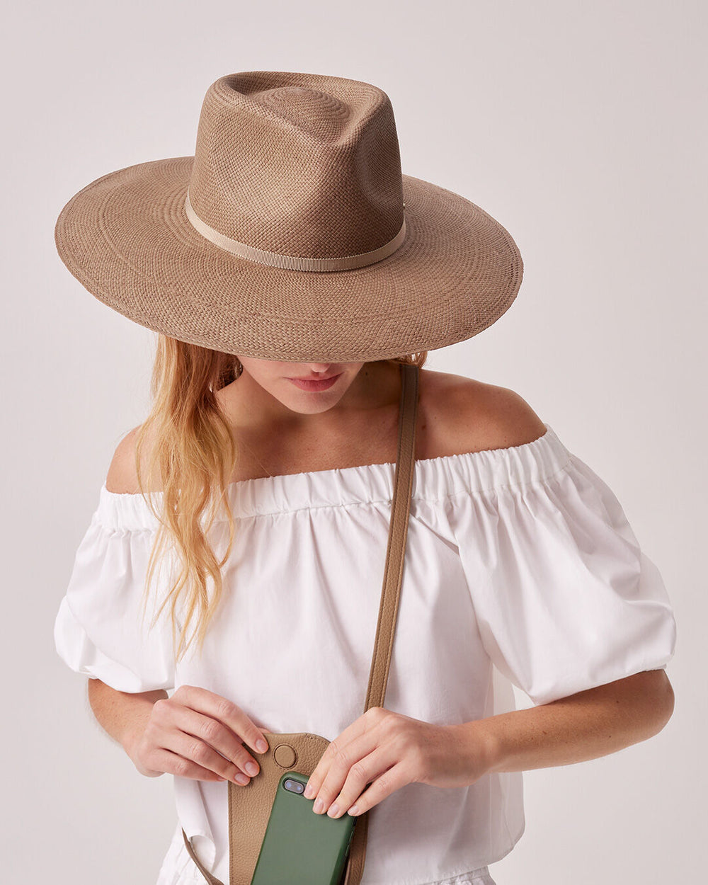 Woman in wide-brimmed hat holding a purse, looking down