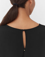 Woman seen from behind showing the back of her top with a keyhole detail and a ponytail.