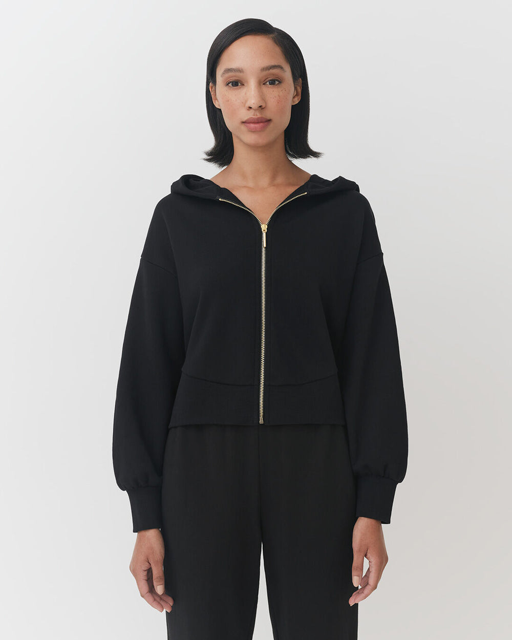 Woman standing in zip-up hoodie and pants, facing camera.