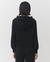 Woman standing from behind, wearing a hoodie with a hood up.
