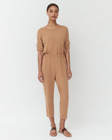 Woman standing in a jumpsuit with sandals, facing forward.