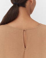 Woman wearing a top with a buttoned keyhole back, ponytail hairstyle.