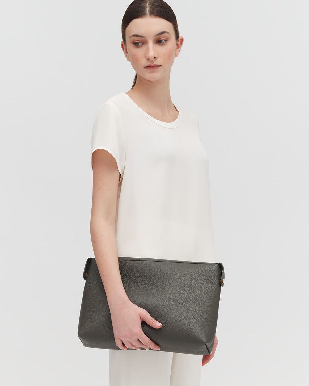 Woman wearing a top and trousers, holding a handbag and standing.