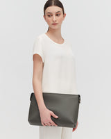 Woman wearing a top and trousers, holding a handbag and standing.