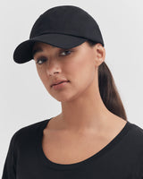 Woman wearing a cap and a crew neck top, looking at the camera.