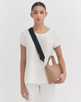 Woman standing with a bag hanging on shoulder strap, looking at camera.
