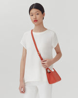 Woman standing with a shoulder bag, looking directly at the camera.