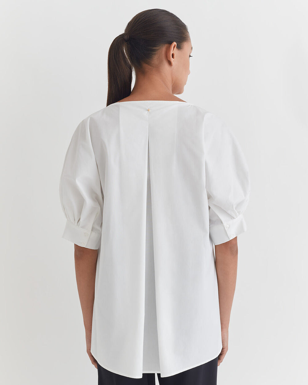 Woman standing with her back facing the camera, wearing a blouse with puffed sleeves.