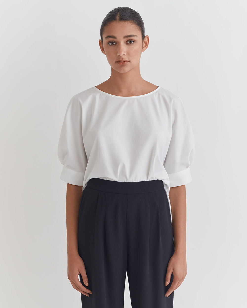 Woman standing in a blouse and pants, looking at the camera.