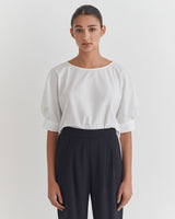 Woman standing in a blouse and pants, looking at the camera.